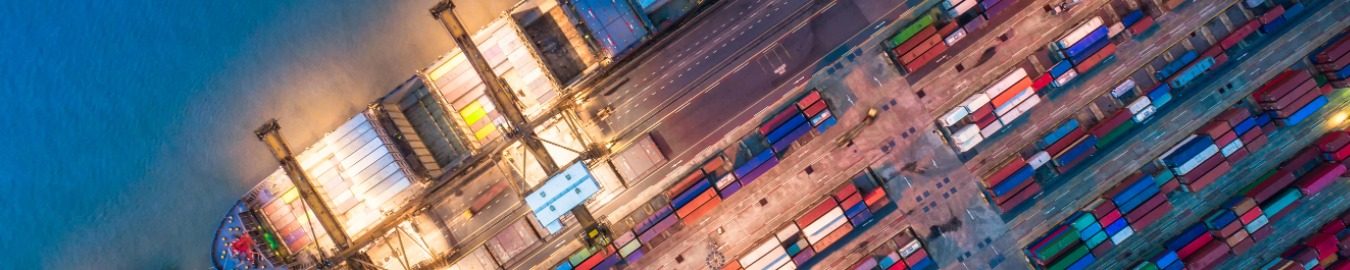 The Geopolitics of Transportation Aerial view of a busy shipping yard with colourful containers and loading cranes.